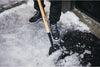 Rimozione della neve con pala Fiskars su vialetto ghiacciato, attrezzo da giardino con manico in legno e punta in metallo, scarpe invernali nere, attrezzatura per la pulizia della neve, strumenti per l'inverno, sicurezza invernale.